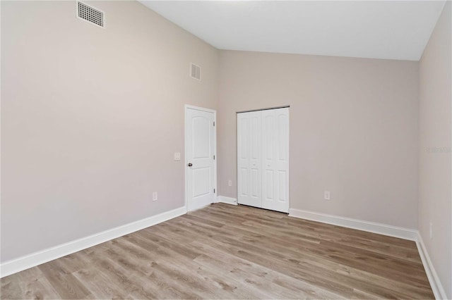 unfurnished bedroom featuring visible vents, baseboards, light wood-style flooring, and vaulted ceiling