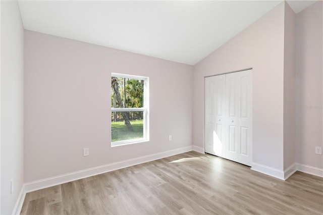 unfurnished bedroom featuring a closet, baseboards, lofted ceiling, and light wood-style floors