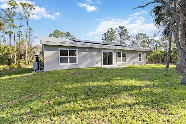 back of property with a yard, solar panels, and stucco siding