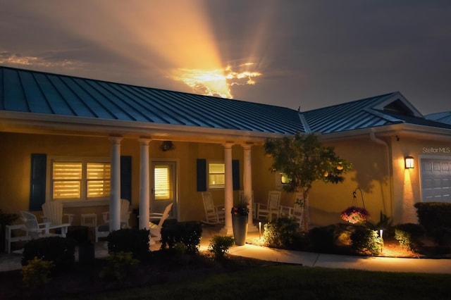 rear view of property featuring metal roof, a garage, covered porch, and a standing seam roof