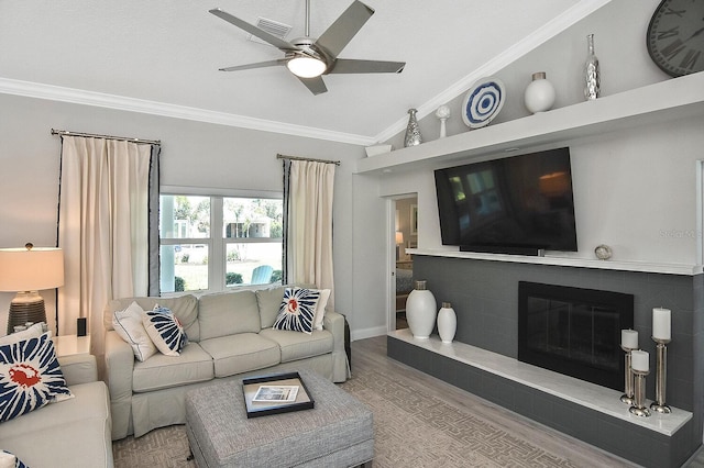 living area featuring a glass covered fireplace, wood finished floors, ornamental molding, and a ceiling fan