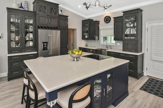 kitchen with light wood-type flooring, high end fridge, ornamental molding, glass insert cabinets, and dark cabinets