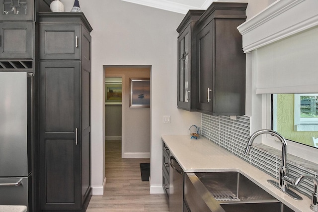 kitchen with light wood-style flooring, a sink, backsplash, appliances with stainless steel finishes, and light countertops