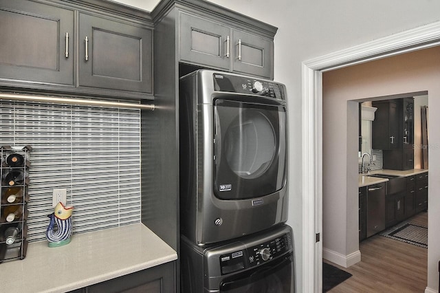 laundry area with cabinet space, stacked washer and dryer, wood finished floors, and a sink