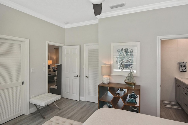 bedroom with visible vents, baseboards, wood finished floors, and ornamental molding