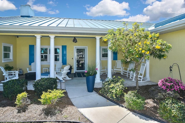 doorway to property with a standing seam roof, metal roof, covered porch, and stucco siding