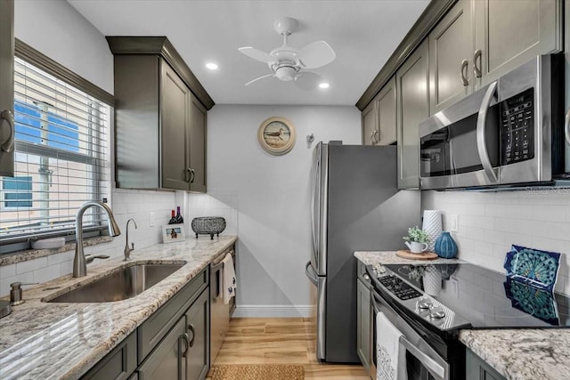 kitchen with appliances with stainless steel finishes, light stone countertops, light wood-type flooring, and a sink