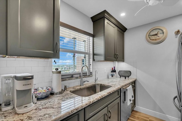 kitchen featuring light stone countertops, baseboards, a sink, stainless steel dishwasher, and tasteful backsplash