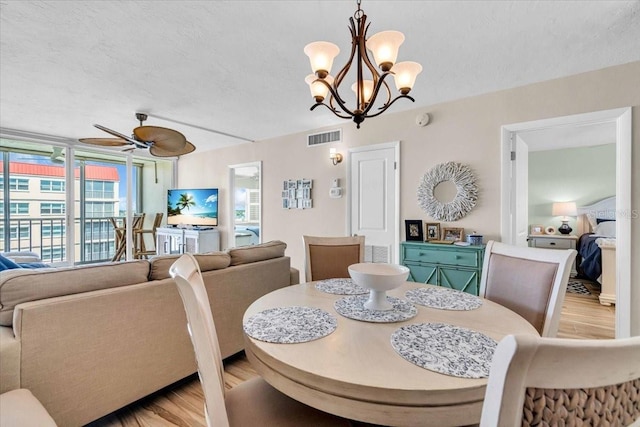 dining area with visible vents, ceiling fan with notable chandelier, a textured ceiling, and light wood-style floors