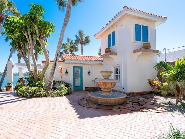 mediterranean / spanish house featuring a water view, stucco siding, and a tiled roof