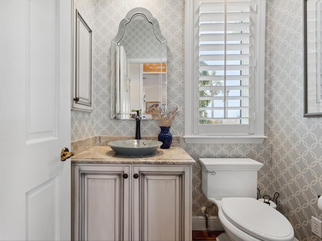 half bathroom with toilet, wallpapered walls, and vanity