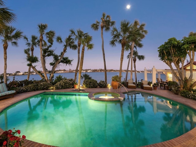 pool at dusk with a water view, a pool with connected hot tub, and a patio area