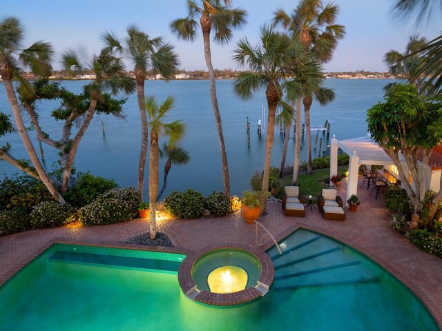 pool at dusk with a water view, a patio, and a pool with connected hot tub