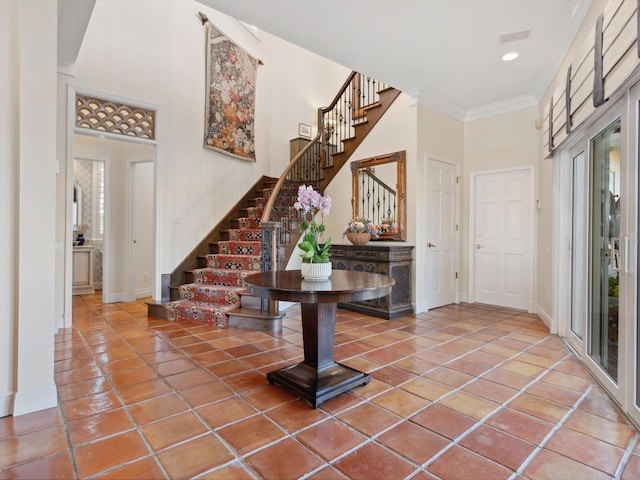 foyer entrance featuring baseboards, a high ceiling, crown molding, stairs, and tile patterned floors