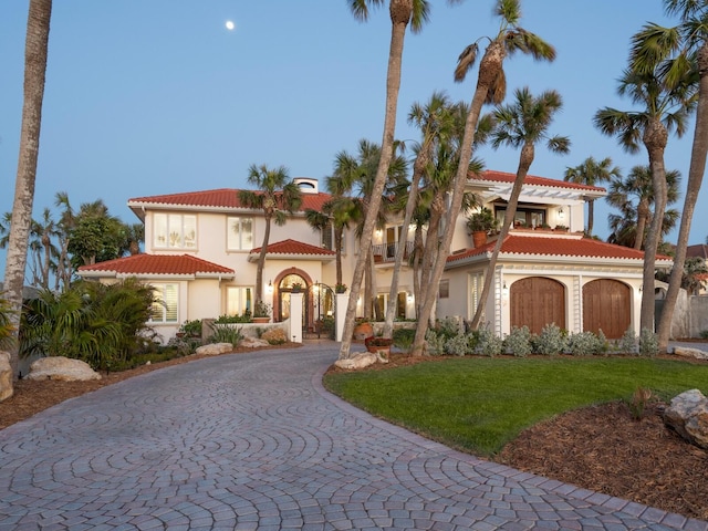 mediterranean / spanish-style house featuring a front yard, a tiled roof, a balcony, curved driveway, and stucco siding