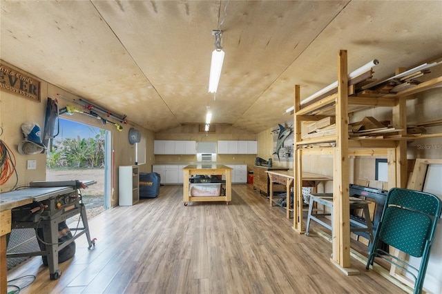 interior space featuring light wood finished floors, a center island, pendant lighting, vaulted ceiling, and white cabinetry