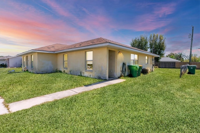 view of home's exterior with stucco siding, a lawn, and fence