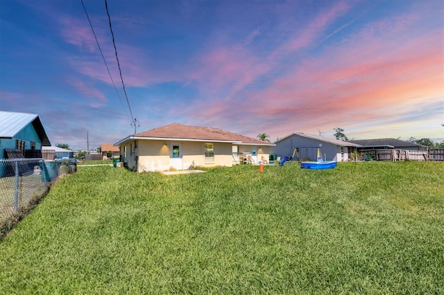 back of property at dusk with a yard, stucco siding, and fence