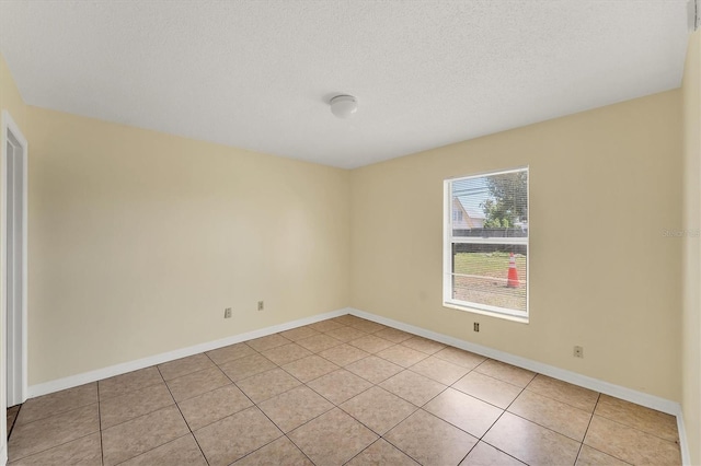 empty room with light tile patterned floors, baseboards, and a textured ceiling