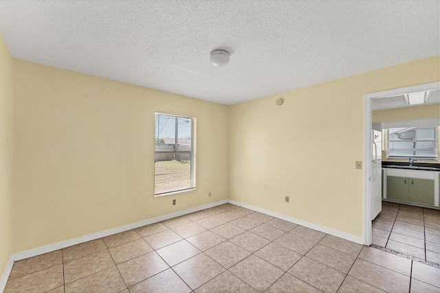 spare room featuring light tile patterned floors, a textured ceiling, baseboards, and a sink