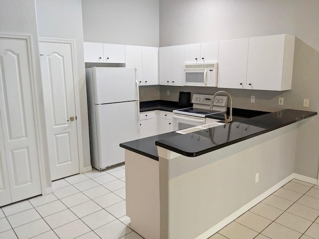 kitchen featuring white appliances, dark countertops, light tile patterned flooring, and a peninsula