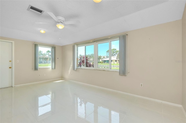 tiled empty room featuring ceiling fan, baseboards, visible vents, and a textured ceiling