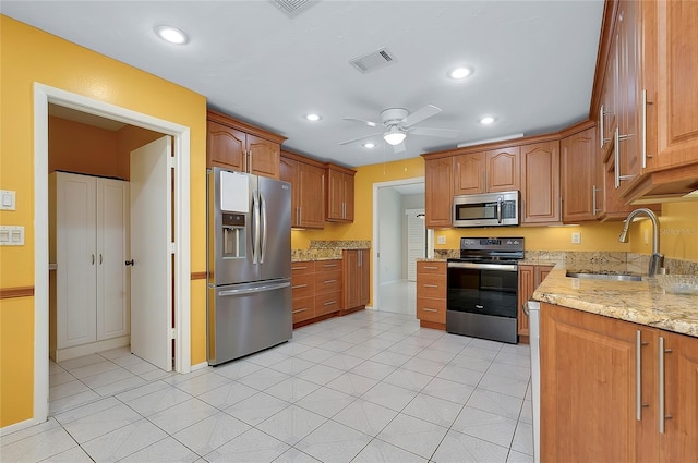 kitchen featuring visible vents, a sink, stainless steel appliances, light stone countertops, and ceiling fan