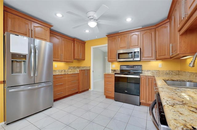 kitchen featuring a sink, light stone countertops, appliances with stainless steel finishes, and a ceiling fan