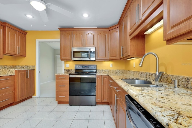 kitchen with a sink, light stone counters, appliances with stainless steel finishes, and ceiling fan