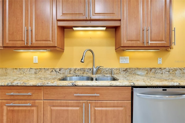 kitchen with stainless steel dishwasher, light stone countertops, and a sink