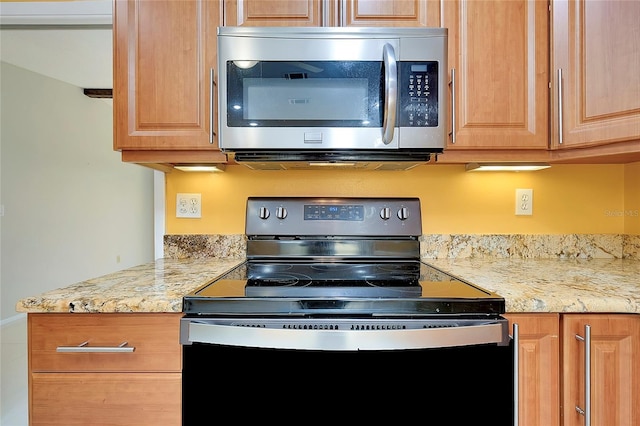 kitchen featuring stainless steel microwave, light stone countertops, and black range with electric stovetop