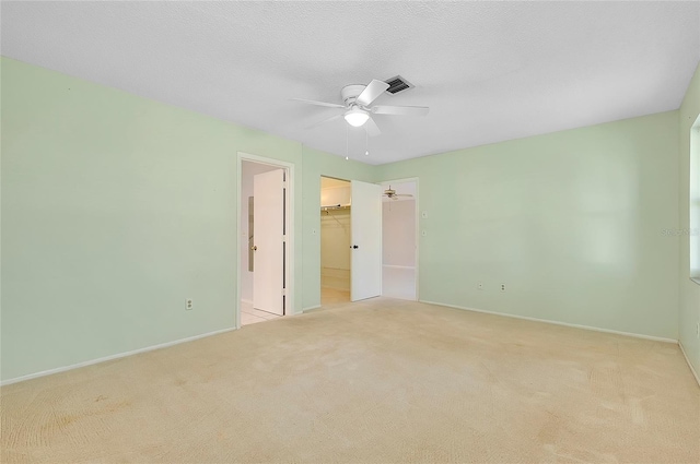 unfurnished bedroom with visible vents, a closet, a textured ceiling, a walk in closet, and light colored carpet