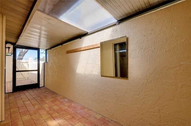 hallway with wooden ceiling, a textured wall, and brick floor