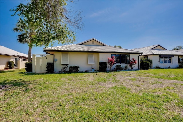 rear view of house with a lawn, a tiled roof, fence, and stucco siding