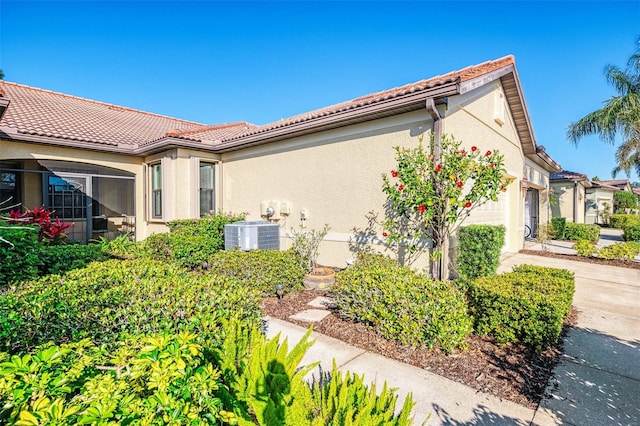 view of home's exterior featuring a tile roof, central AC unit, stucco siding, driveway, and an attached garage