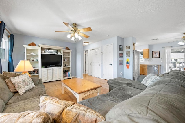 living area with light wood finished floors, visible vents, a textured ceiling, and a ceiling fan