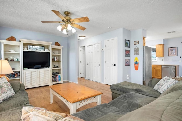 living area with ceiling fan, visible vents, a textured ceiling, and light wood-style flooring