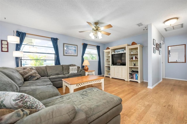 living area with a ceiling fan, light wood-style floors, visible vents, and a textured ceiling