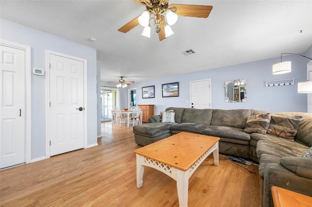 living room with light wood finished floors, visible vents, a textured ceiling, and ceiling fan