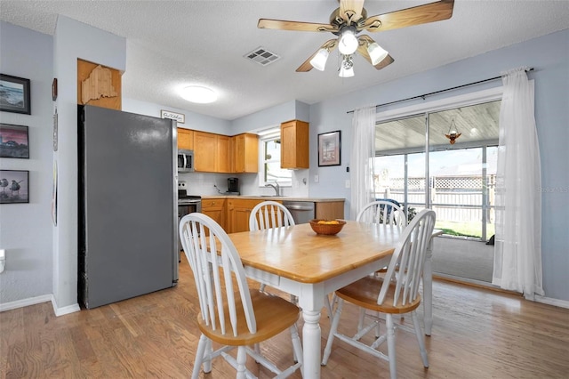 dining area featuring visible vents, a textured ceiling, light wood-style floors, baseboards, and ceiling fan