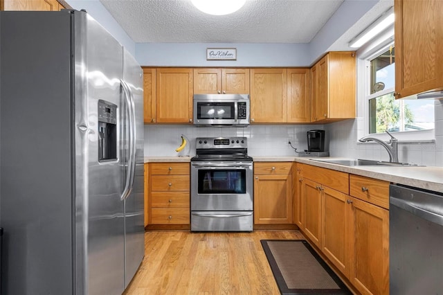 kitchen with light wood finished floors, backsplash, light countertops, appliances with stainless steel finishes, and a sink