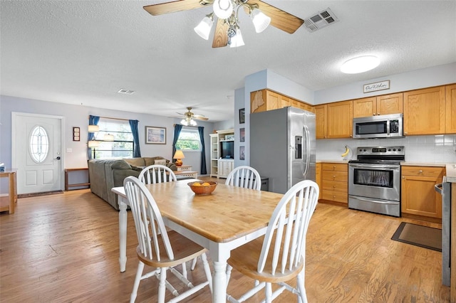 dining room with light wood finished floors, visible vents, a textured ceiling, and ceiling fan