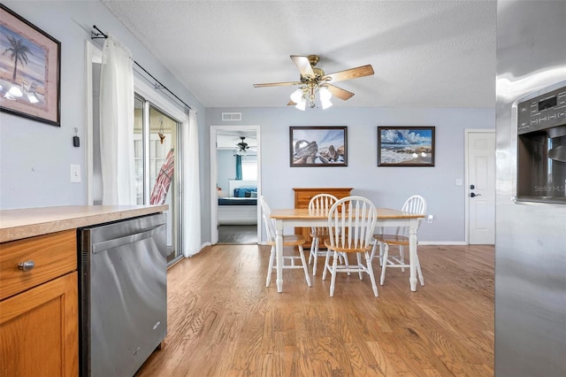 dining area with visible vents, baseboards, light wood-type flooring, a textured ceiling, and a ceiling fan