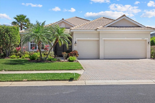 view of front of house with stucco siding, decorative driveway, a front yard, an attached garage, and a tiled roof