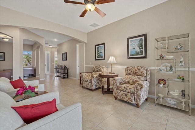 living room featuring visible vents, arched walkways, light tile patterned floors, baseboards, and ceiling fan