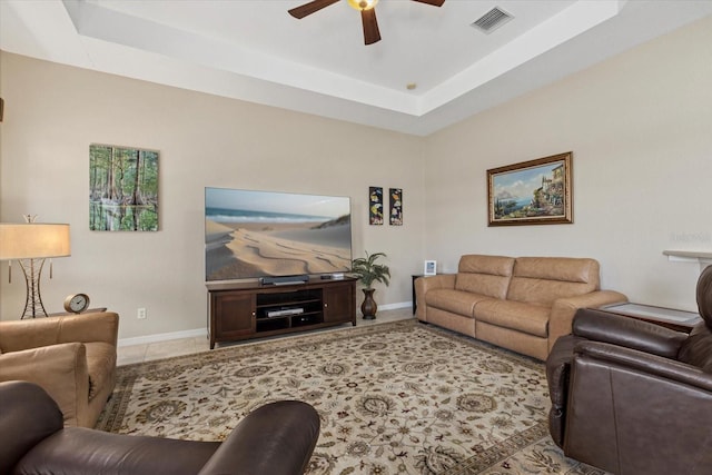 living room with a tray ceiling, visible vents, baseboards, and ceiling fan