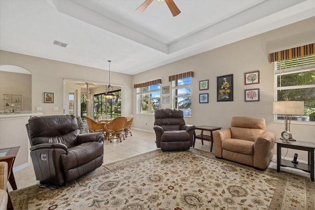 living room with tile patterned floors, visible vents, a ceiling fan, baseboards, and a raised ceiling