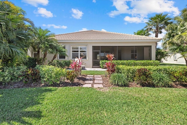 rear view of house with a tiled roof, a yard, stucco siding, and a sunroom