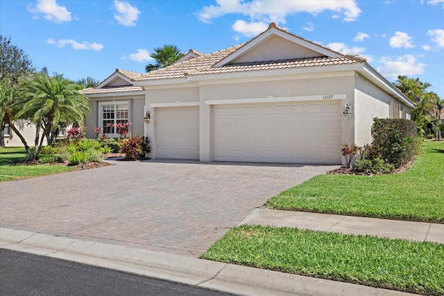 view of front of house featuring a front lawn, a tiled roof, stucco siding, decorative driveway, and an attached garage