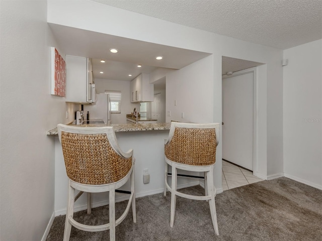 kitchen featuring a peninsula, light tile patterned flooring, recessed lighting, a textured ceiling, and a kitchen bar